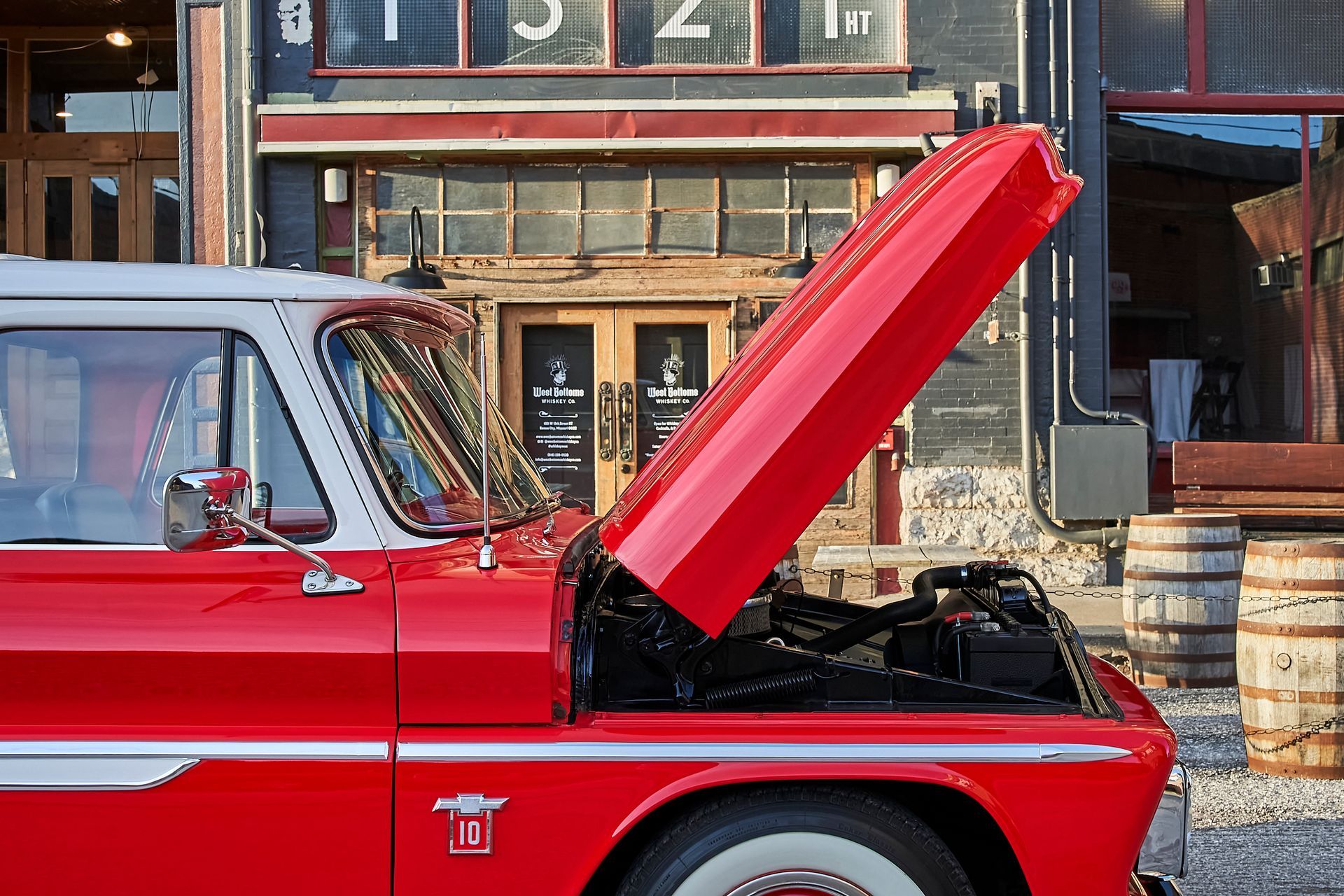 A red truck with its hood open is parked in front of a building.