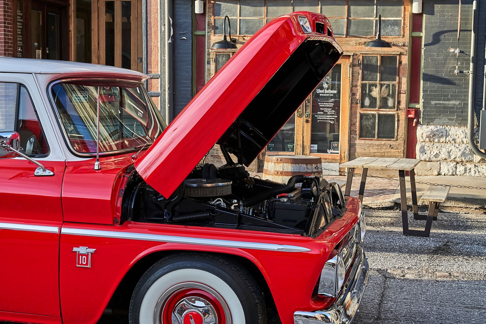 A red truck with the hood up is parked in front of a building.