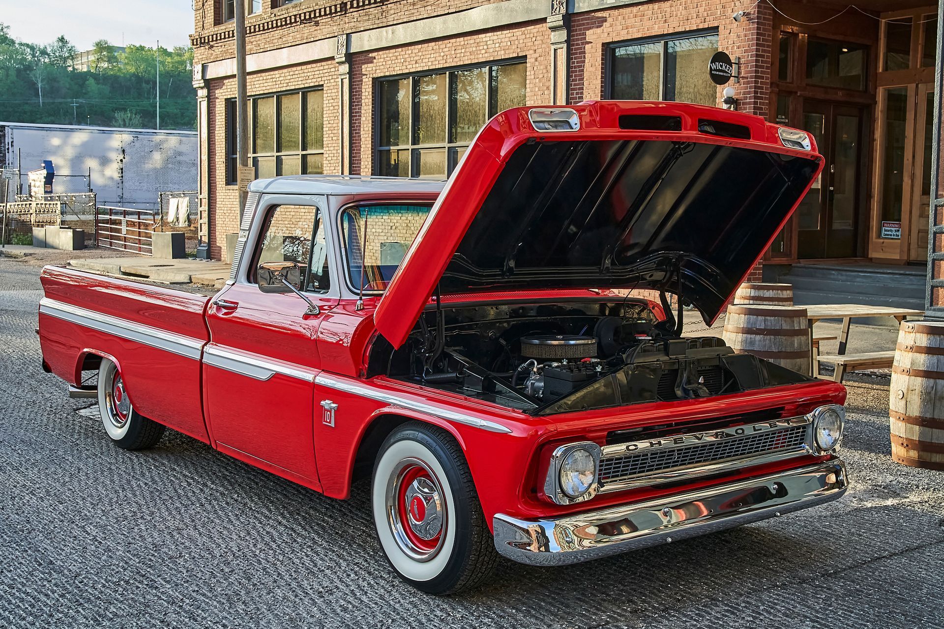 A red truck with the hood up is parked in front of a building.