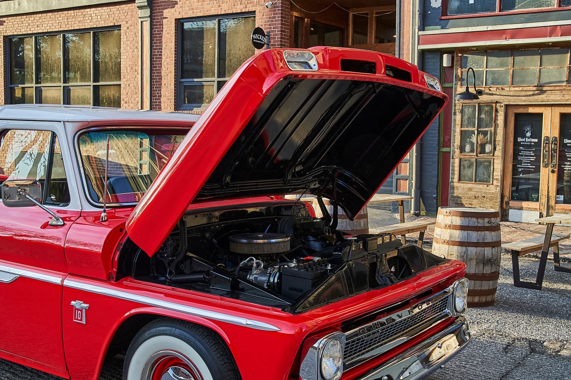 A red truck with its hood open is parked in front of a building.