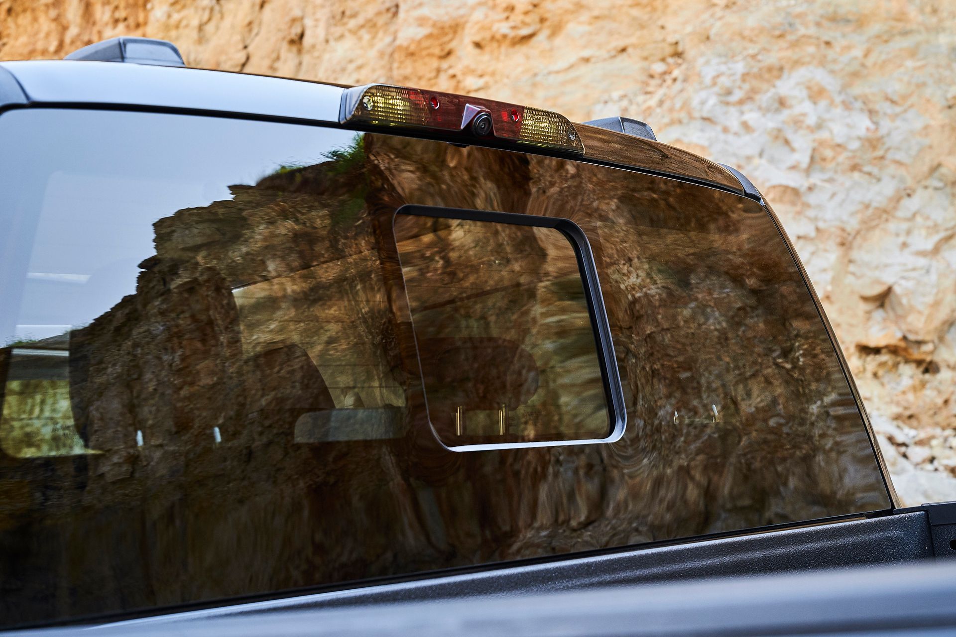 The back window of a truck with a reflection of a mountain in it.