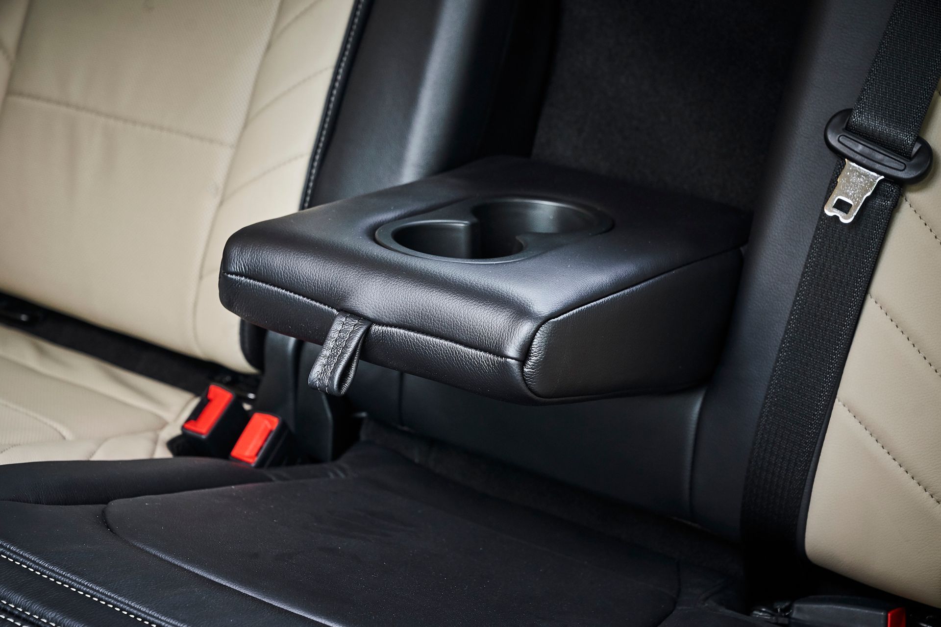 A black arm rest with a cup holder in the back seat of a car.