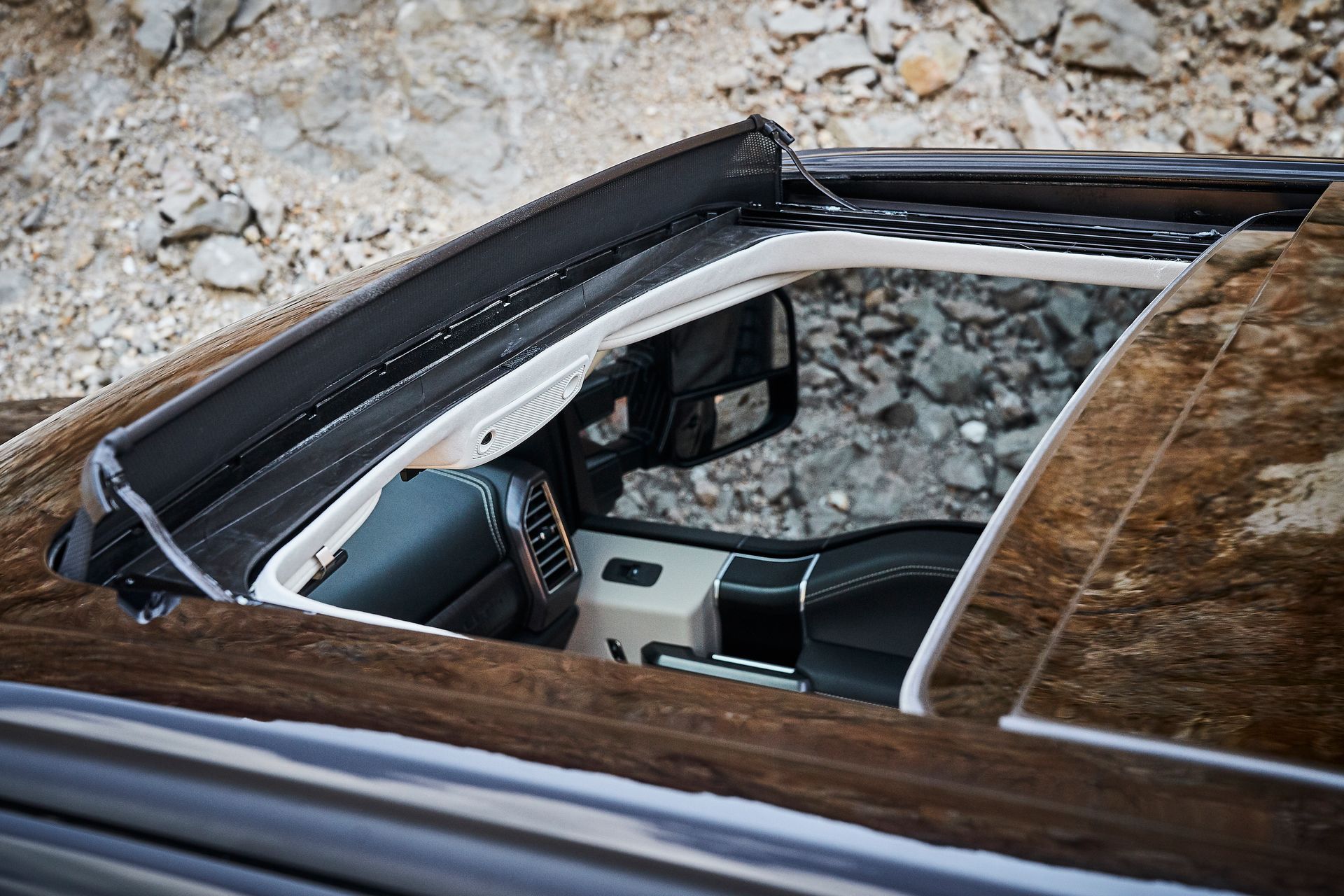The sunroof of a car is open and sitting on top of a pile of rocks.