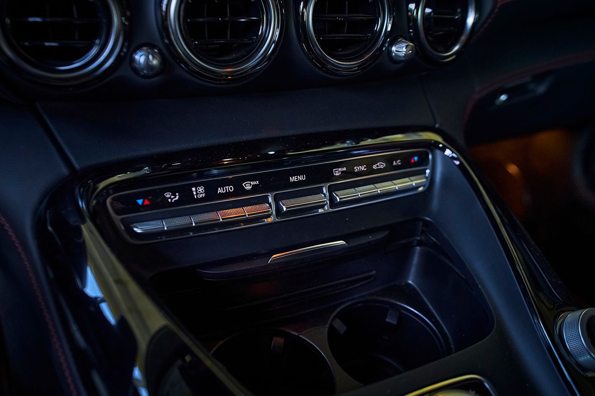 A close up of a car dashboard with a climate control and a cup holder.