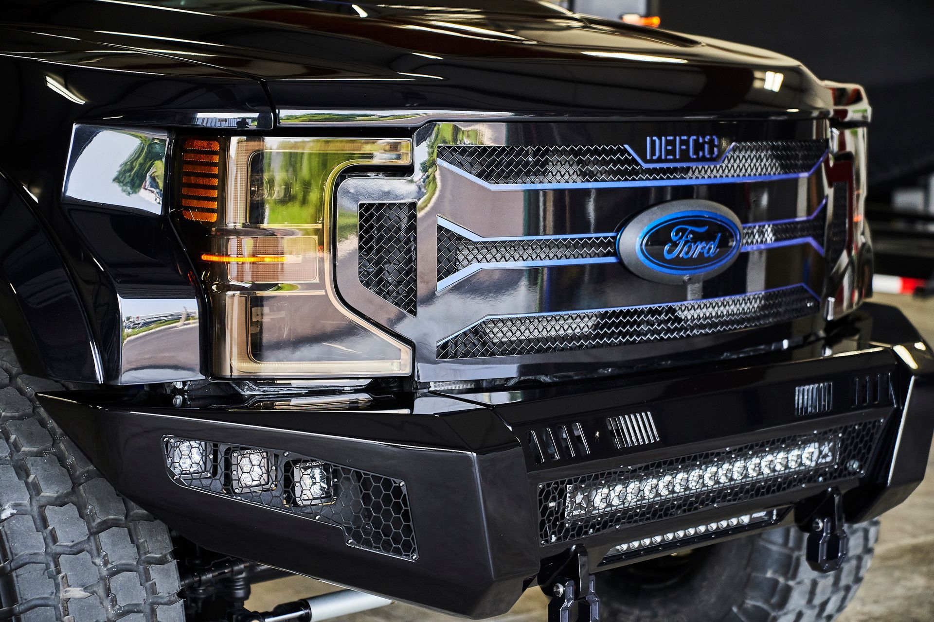 A black ford truck with a grille and bumper is parked in a garage.