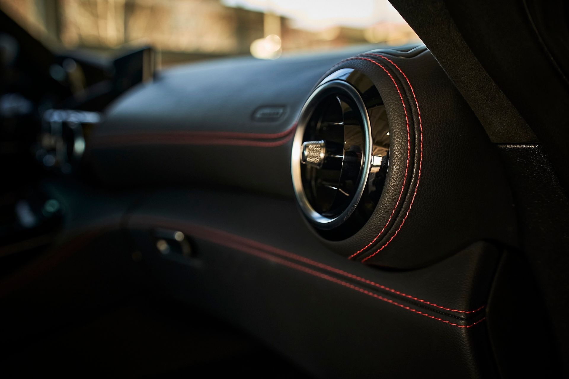 A close up of a car air vent with red stitching.