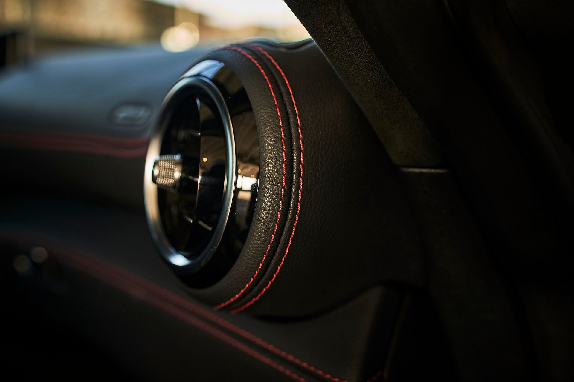 A close up of a car air vent with red stitching.