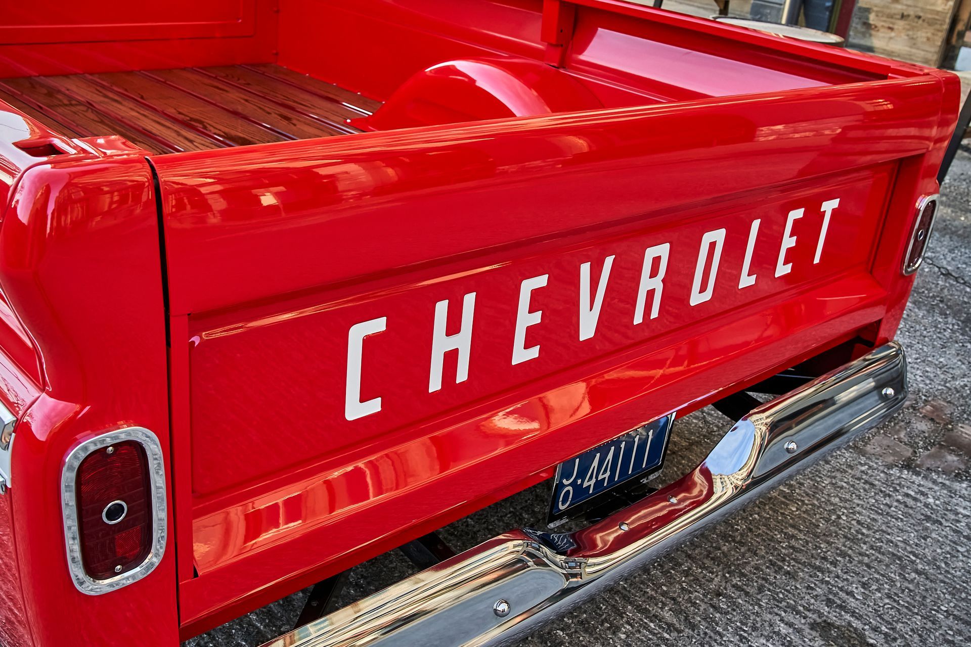 The back of a red chevrolet truck with a wooden bed