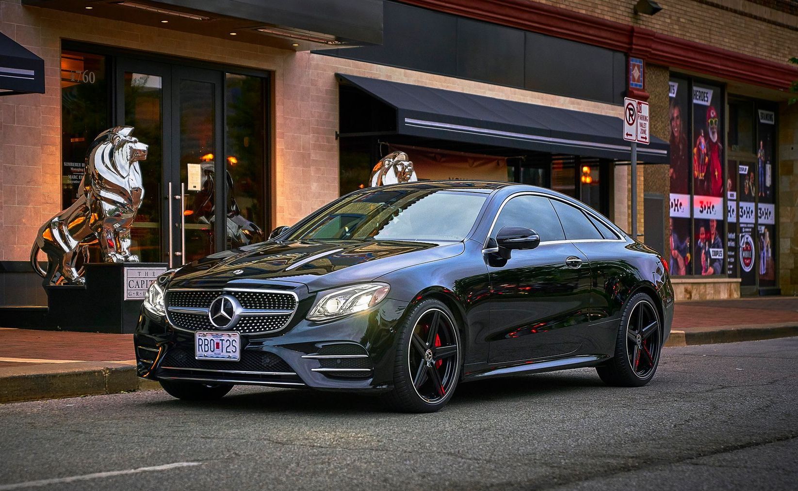 A black mercedes benz e class coupe is parked on the side of the road in front of a building.