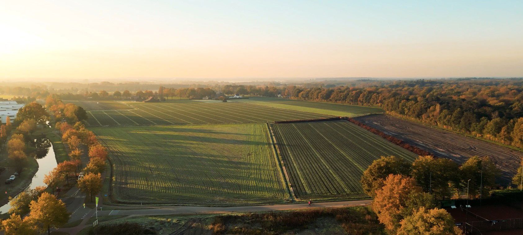 Een luchtfoto van een veld en een rivier bij zonsondergang.