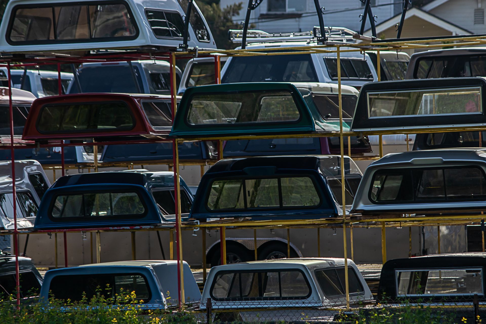 Truck bed toppers stacked on metal racks, various colors, outdoor setting.
