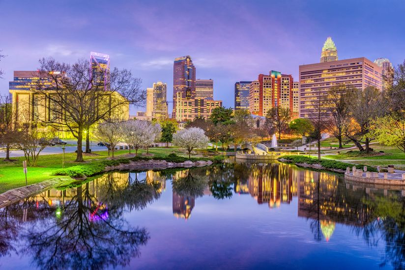 A city skyline is reflected in a lake in a park.