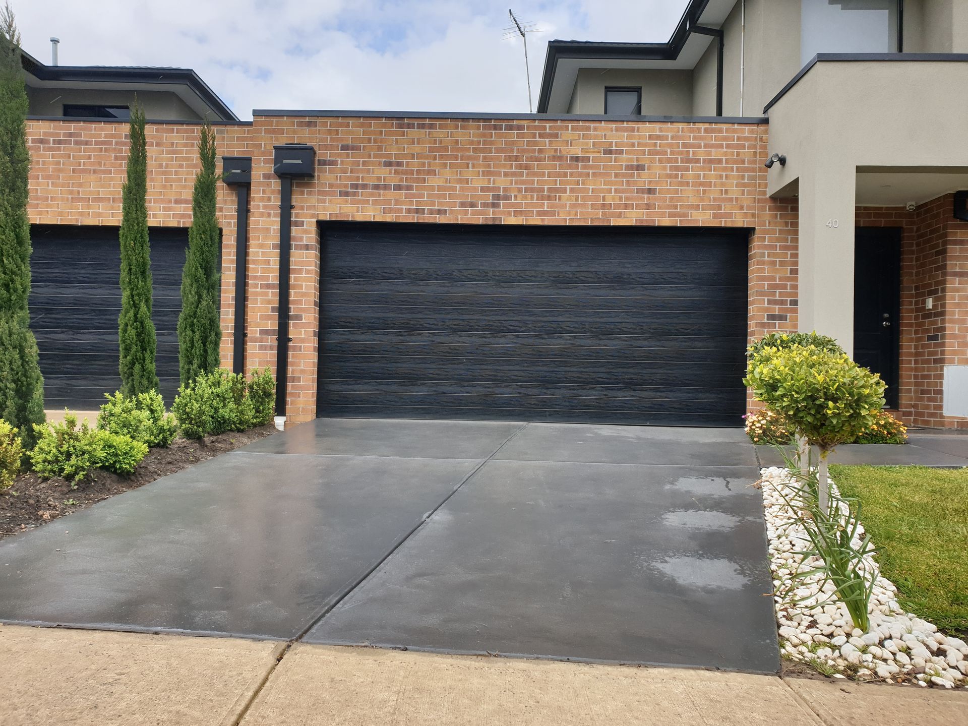 Modern house exterior with black garage door, brick facade, and wet driveway