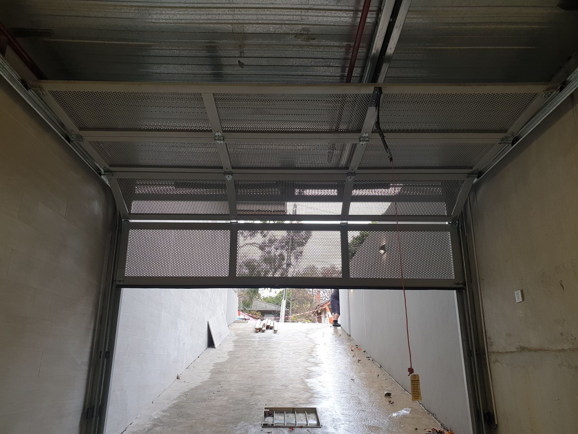 Covered driveway ramp with wet pavement, white walls, and metal gate overhead.