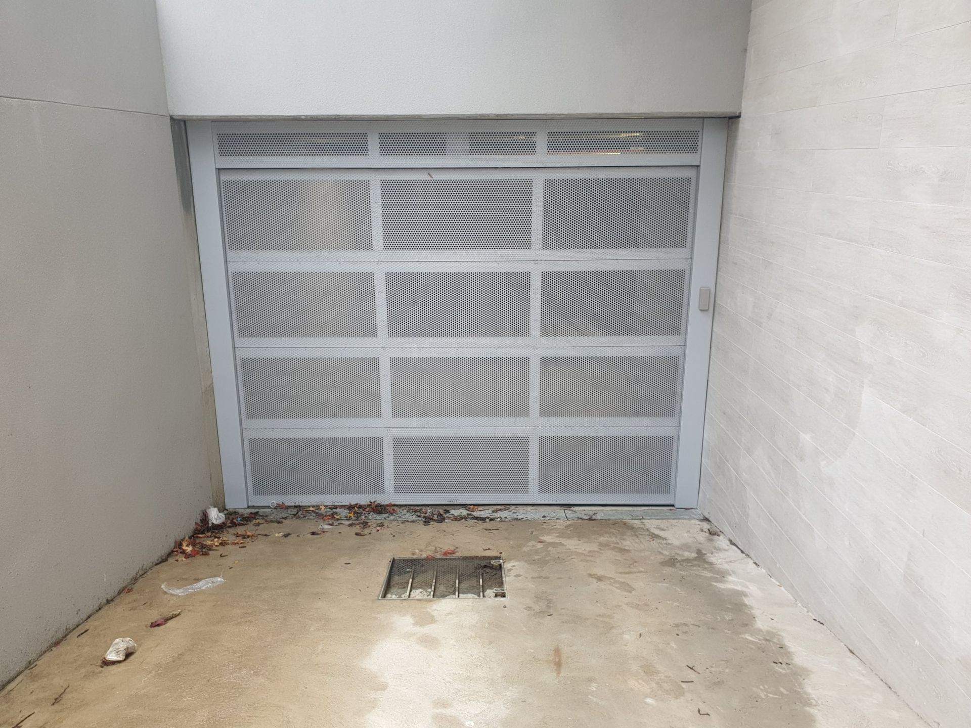Empty concrete driveway facing a gray metal garage door in a narrow alcove