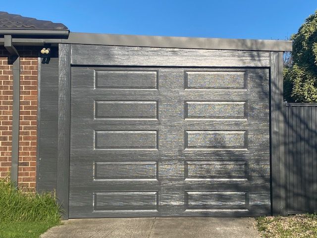 Gray paneled garage door on a brick house in sunlight