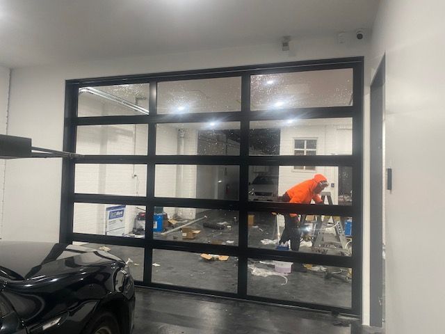 Person in orange jacket working in a garage behind glass-paneled doors