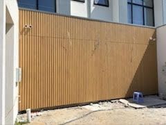 Tan corrugated metal gate or wall with a blue stool beside it and concrete ground below