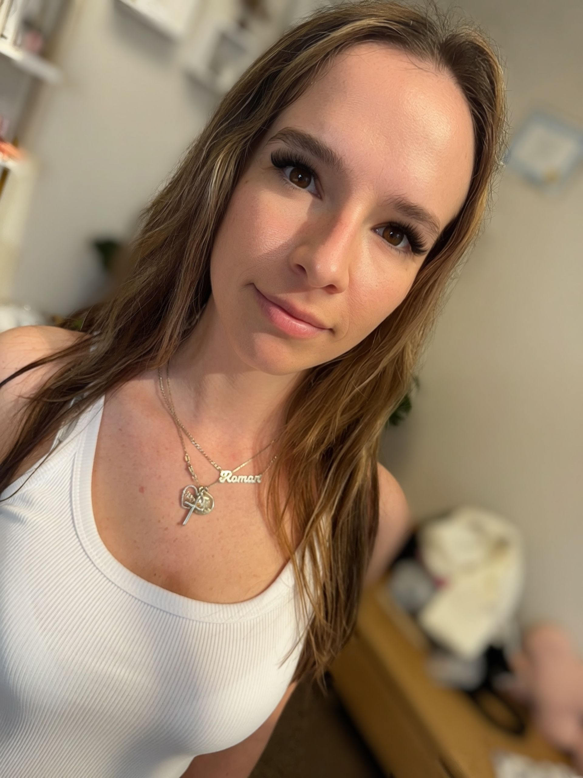 Woman in a white tank top, looking at the camera, wearing a necklace.