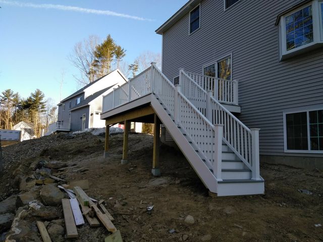 A white deck with stairs leading up to it in front of a house.