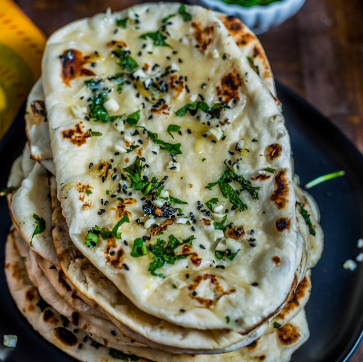 Un gros plan d'une pile de pain naan sur une assiette noire.