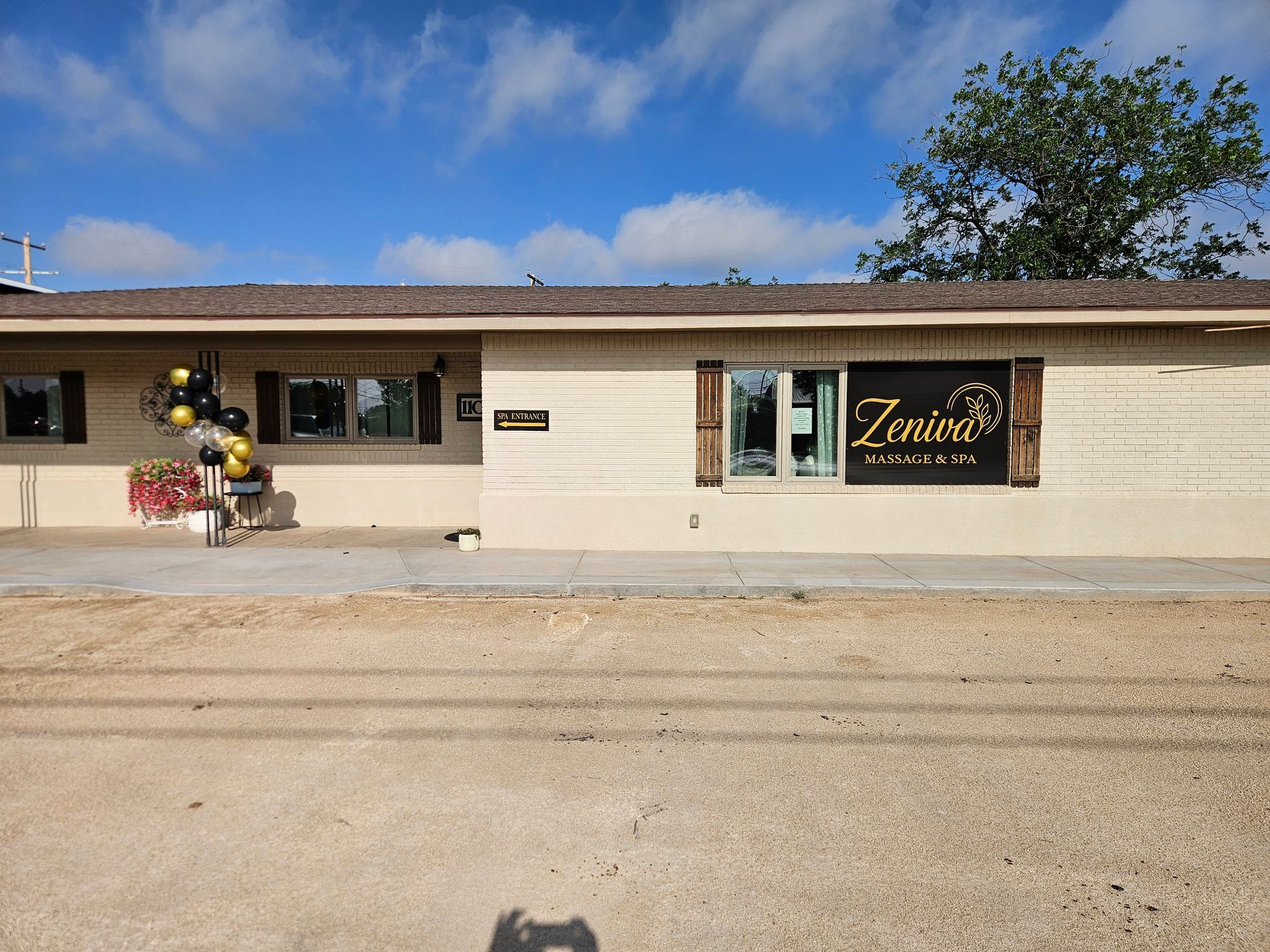 Small beige building with a storefront sign, balloons at the entrance, and a clear blue sky above.