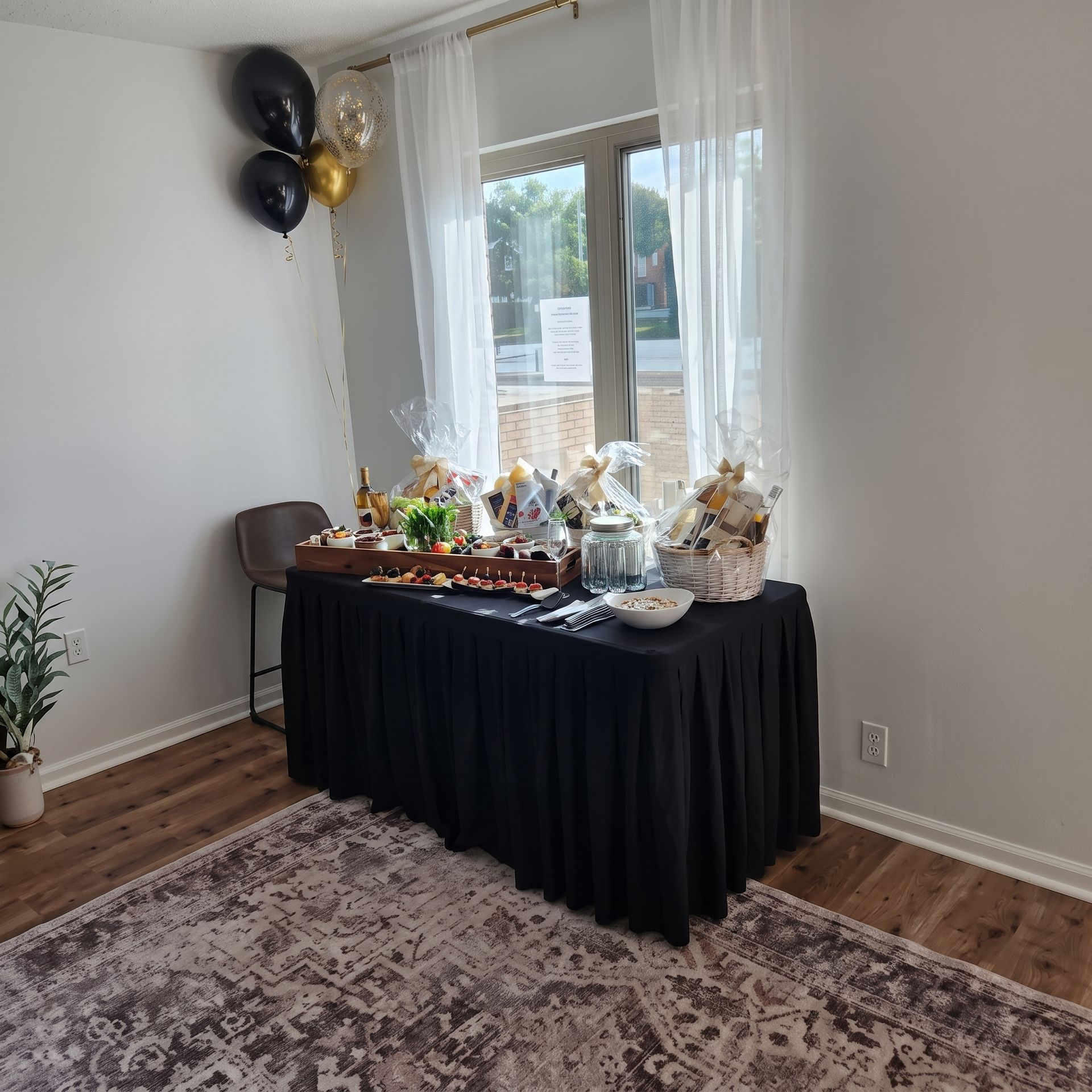 Decorated party dessert table by a window with black tablecloth, balloons, and treats in a bright room