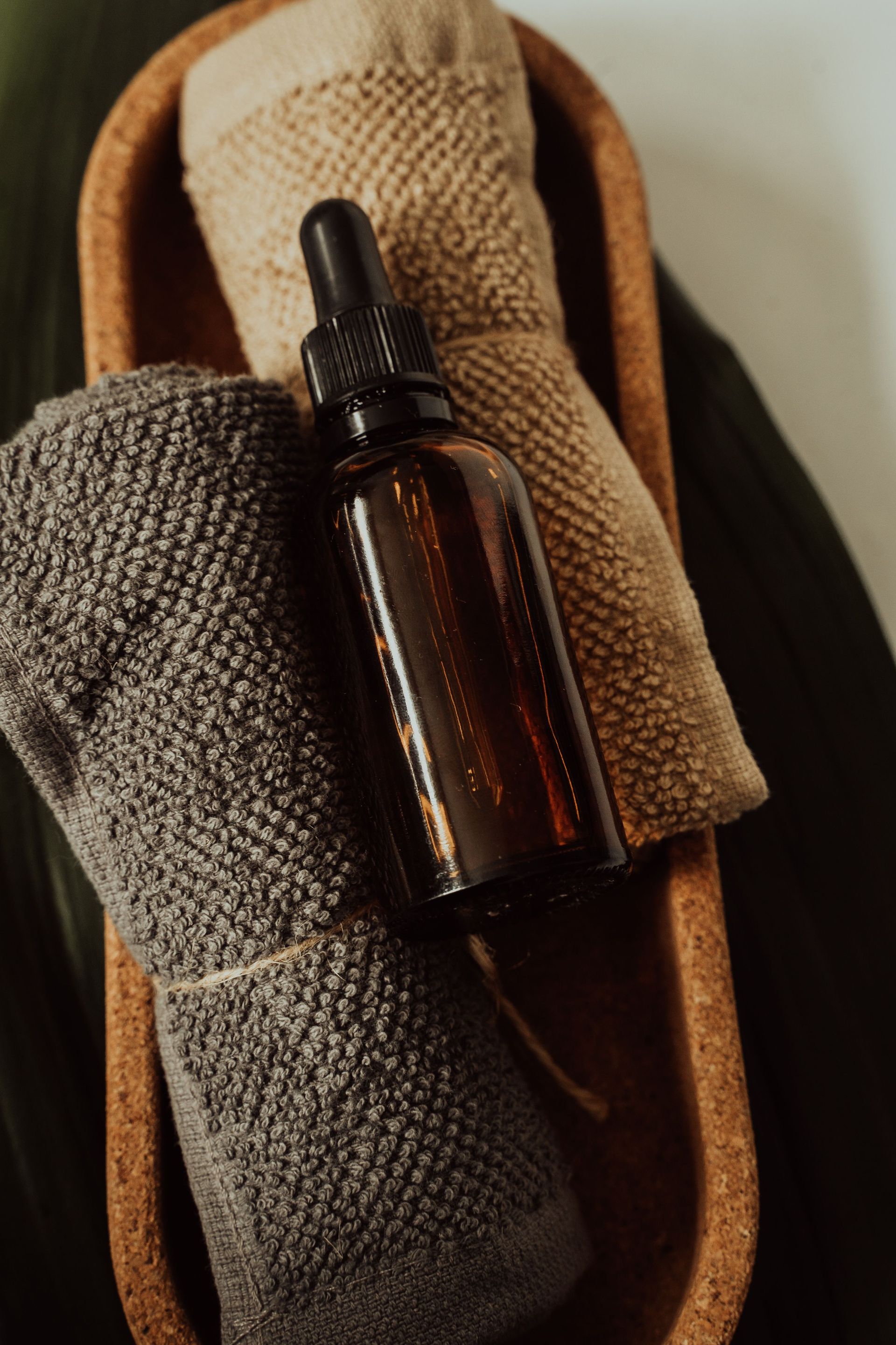 Amber dropper bottle resting on folded brown and beige towels in a wooden tray