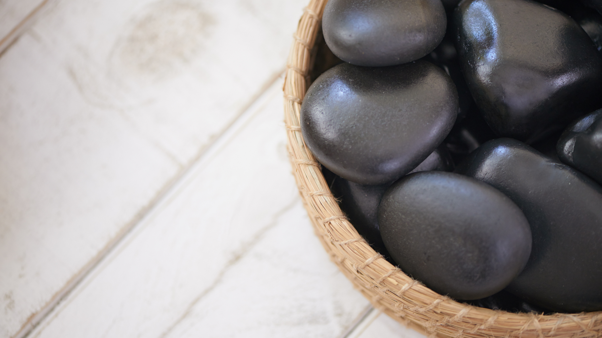 Smooth black stones in a woven basket on a white tiled surface