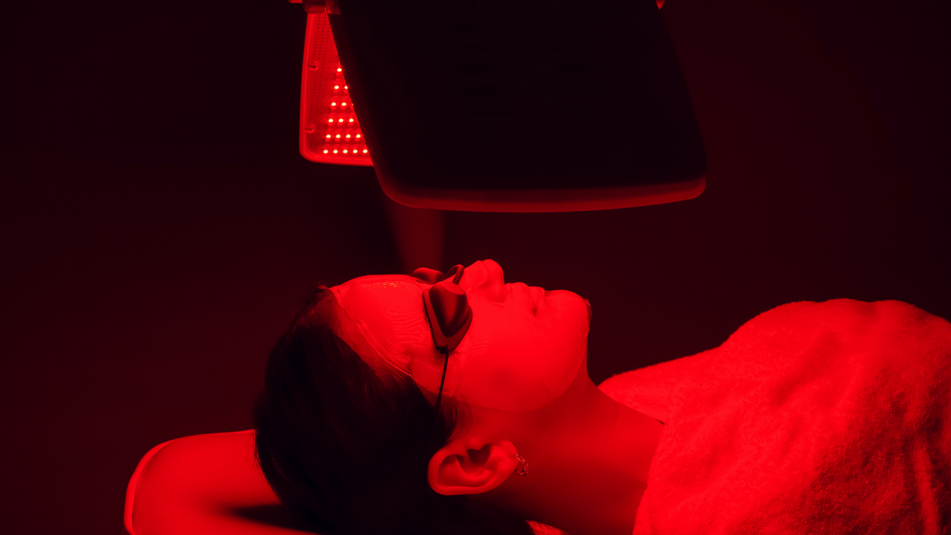 Person lying under a red light with their head tilted back, possibly undergoing a treatment or exam