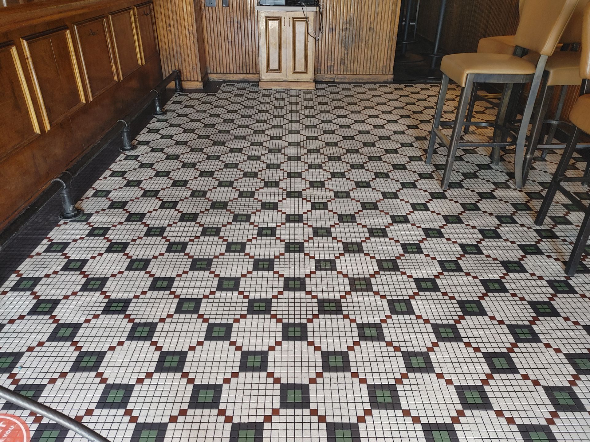 Hand scrubbing diamond-patterned floor tiles with a brush, revealing a clean surface.