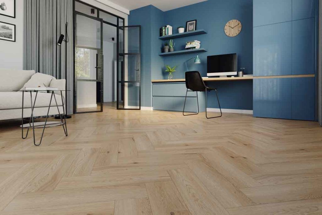 Modern office space with blue walls, herringbone wood floor, desk, and glass door.