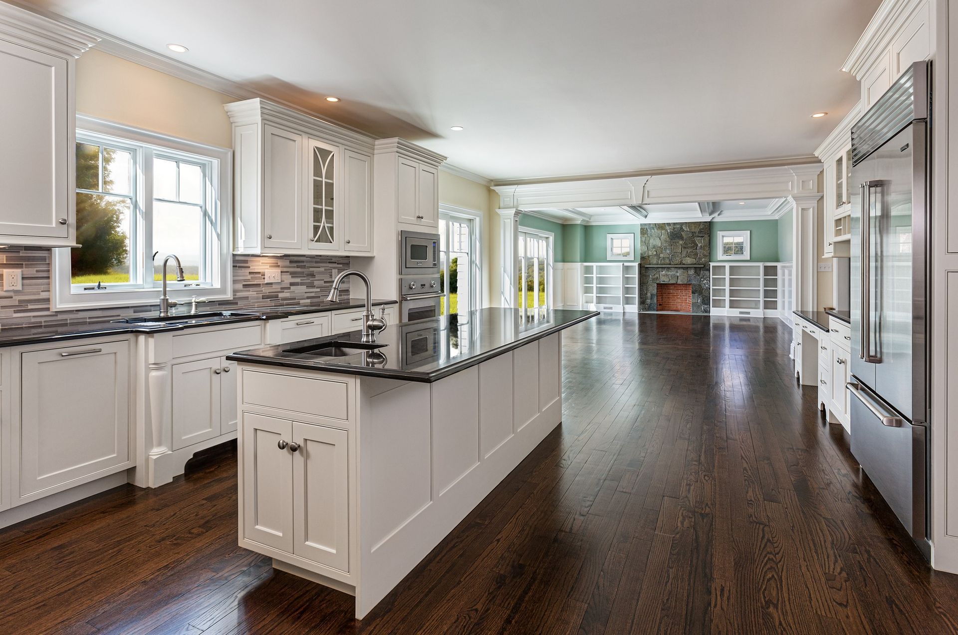 White kitchen with dark wood floors, island, and connected living area with fireplace and built-in shelving.