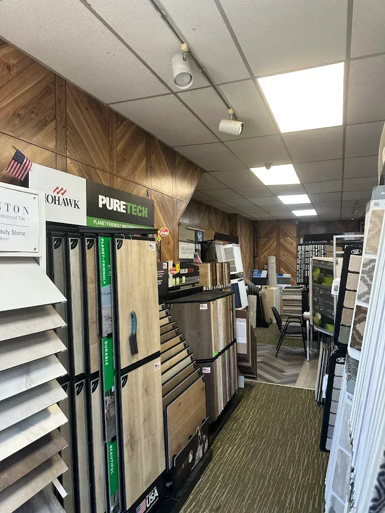 Inside a tile showroom, display racks with tile samples line the aisle, overhead track lighting.