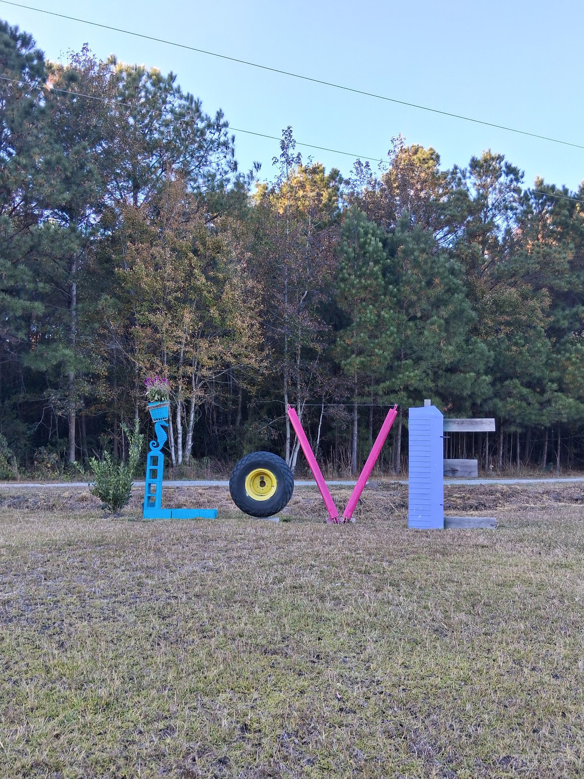 Large, colorful objects arranged to spell LOVE in a grassy field with trees in the background.