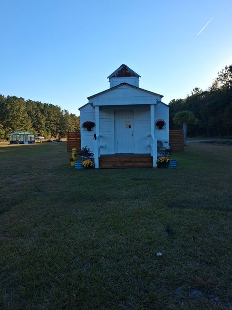 A small, white, chapel-style building with a steeple and wooden steps, set in a sunny, grassy field. A small, white, chapel-style building with a steeple and wooden steps, set in a sunny, grassy field.