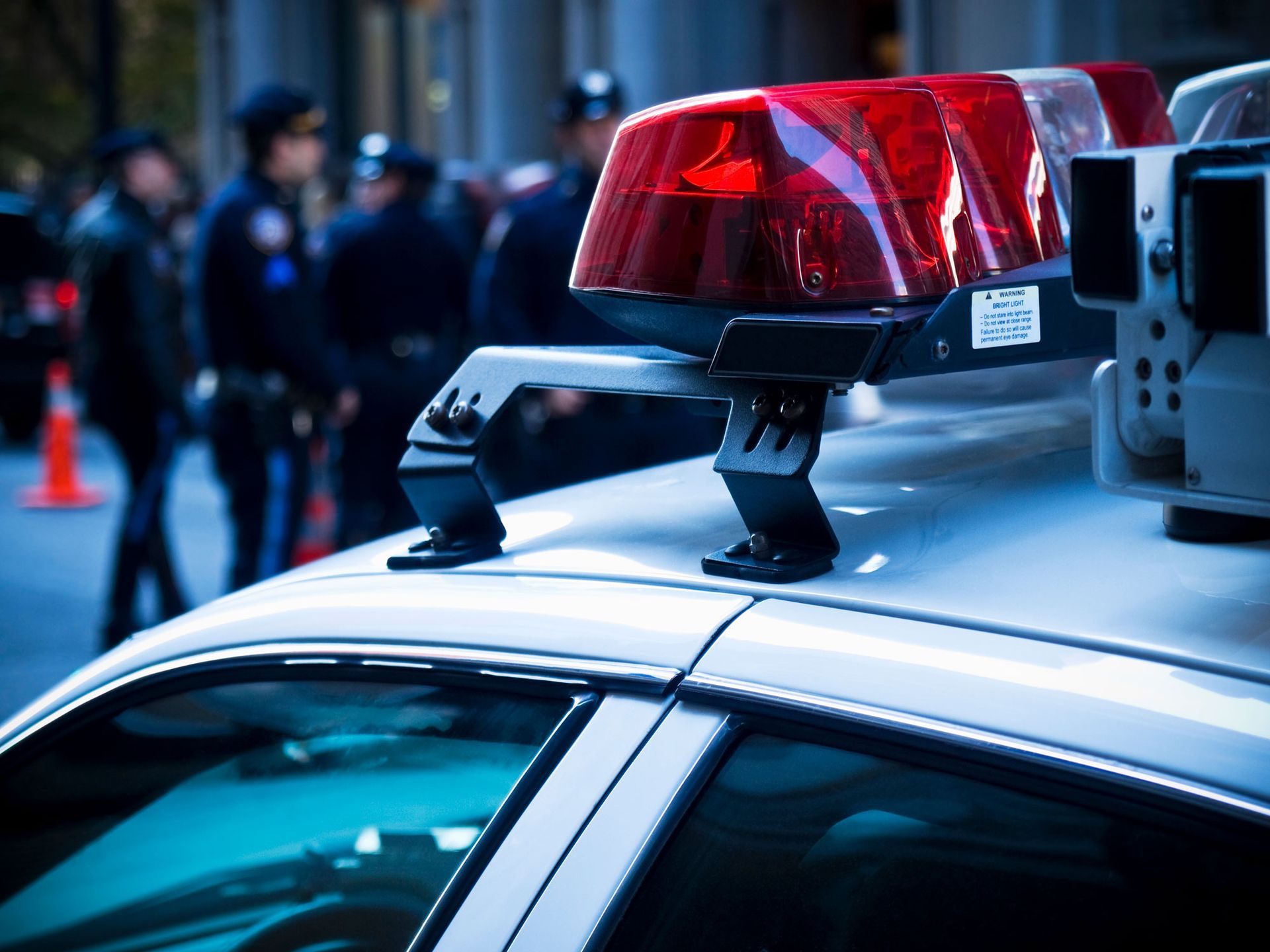 Police car with flashing red lights, officers in background.