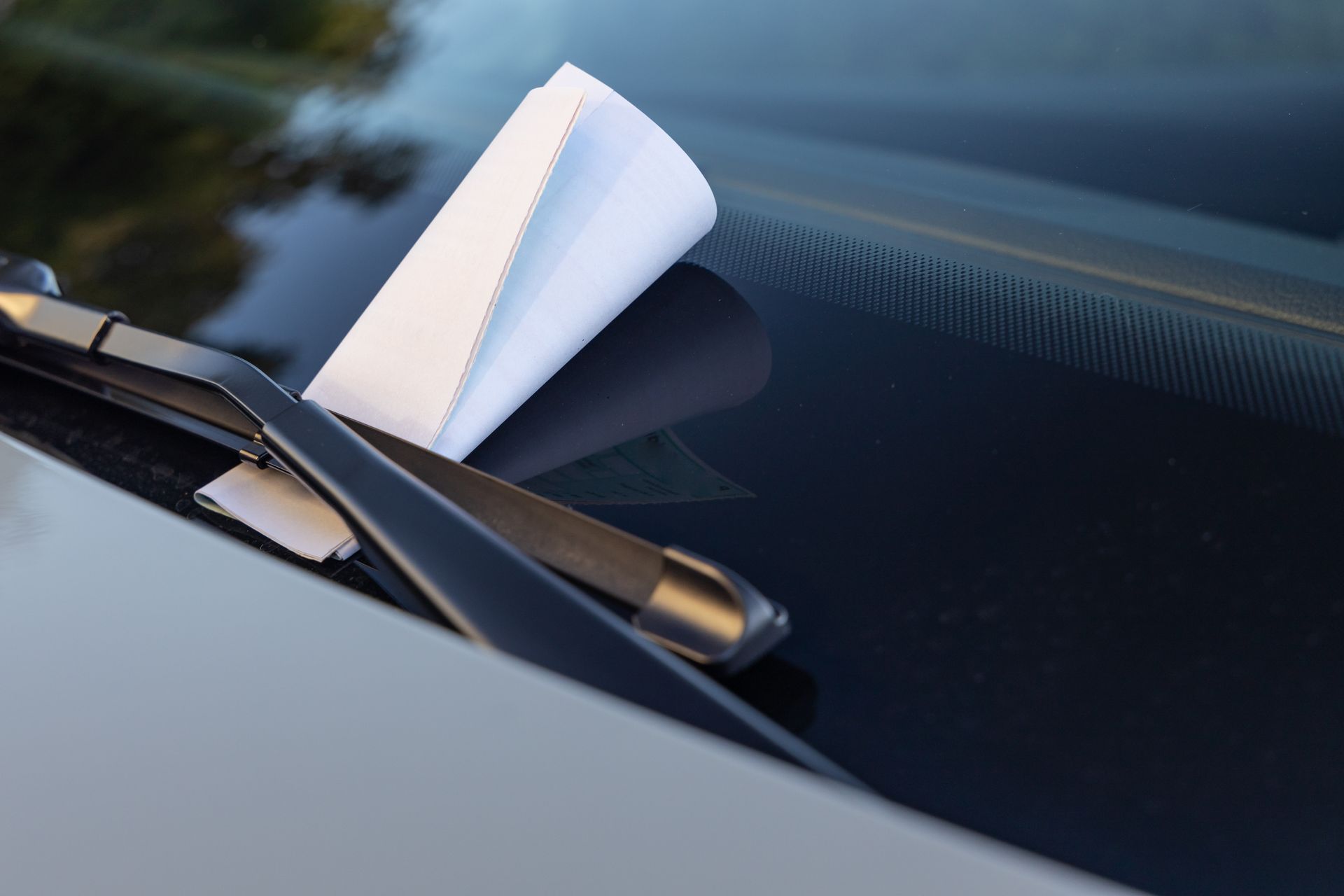 Paper notice tucked under a windshield wiper, indicating a parking ticket.