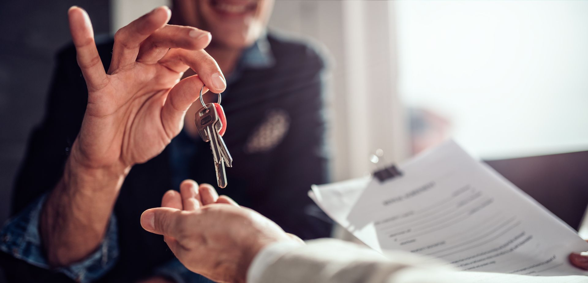 Person handing over keys to another person, paperwork visible.
