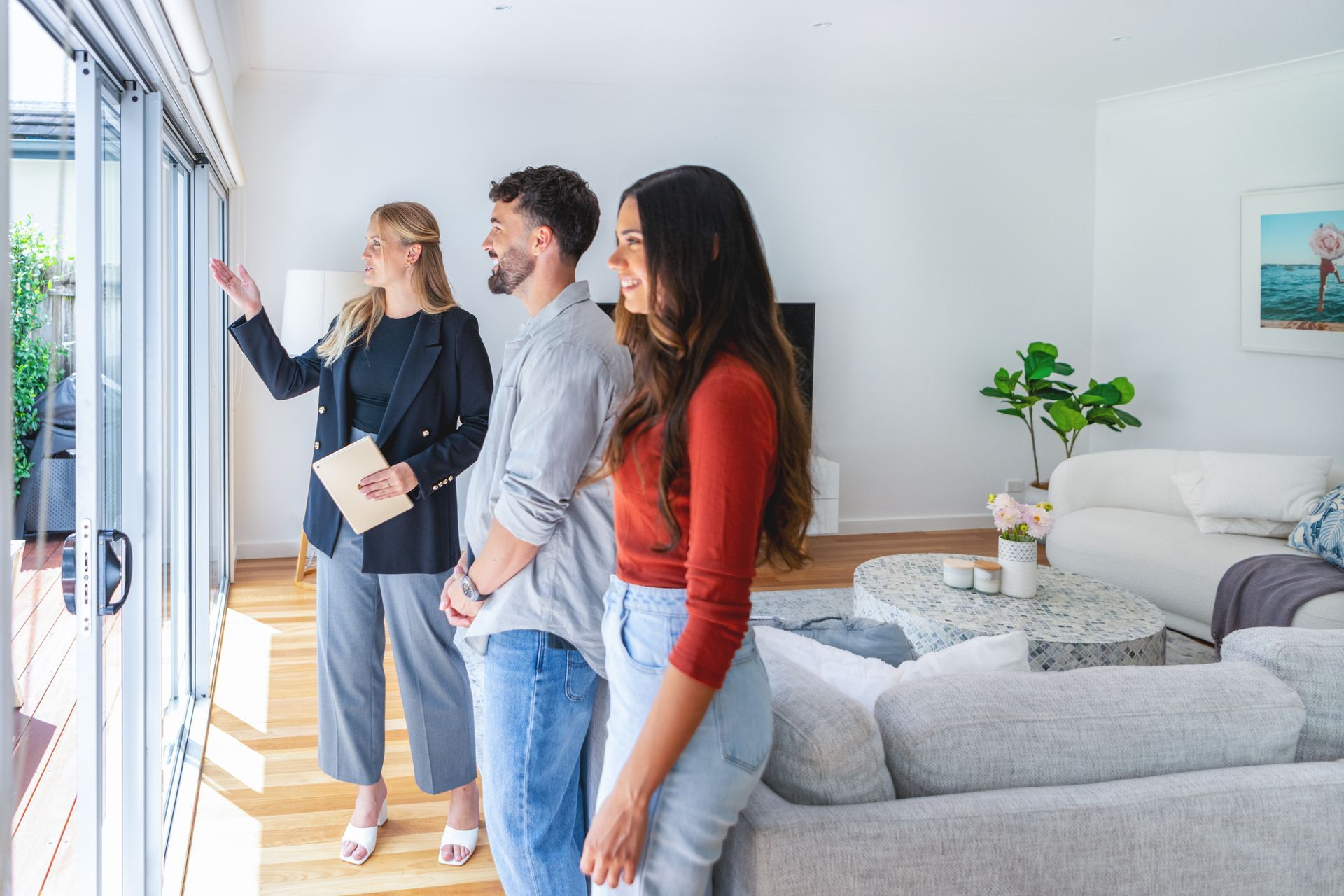A Landlord showing a couple through a new house. They are standing in the living room. She is showing the outdoor area through a window A Landlord showing a couple through a new house. They are standing in the living room.