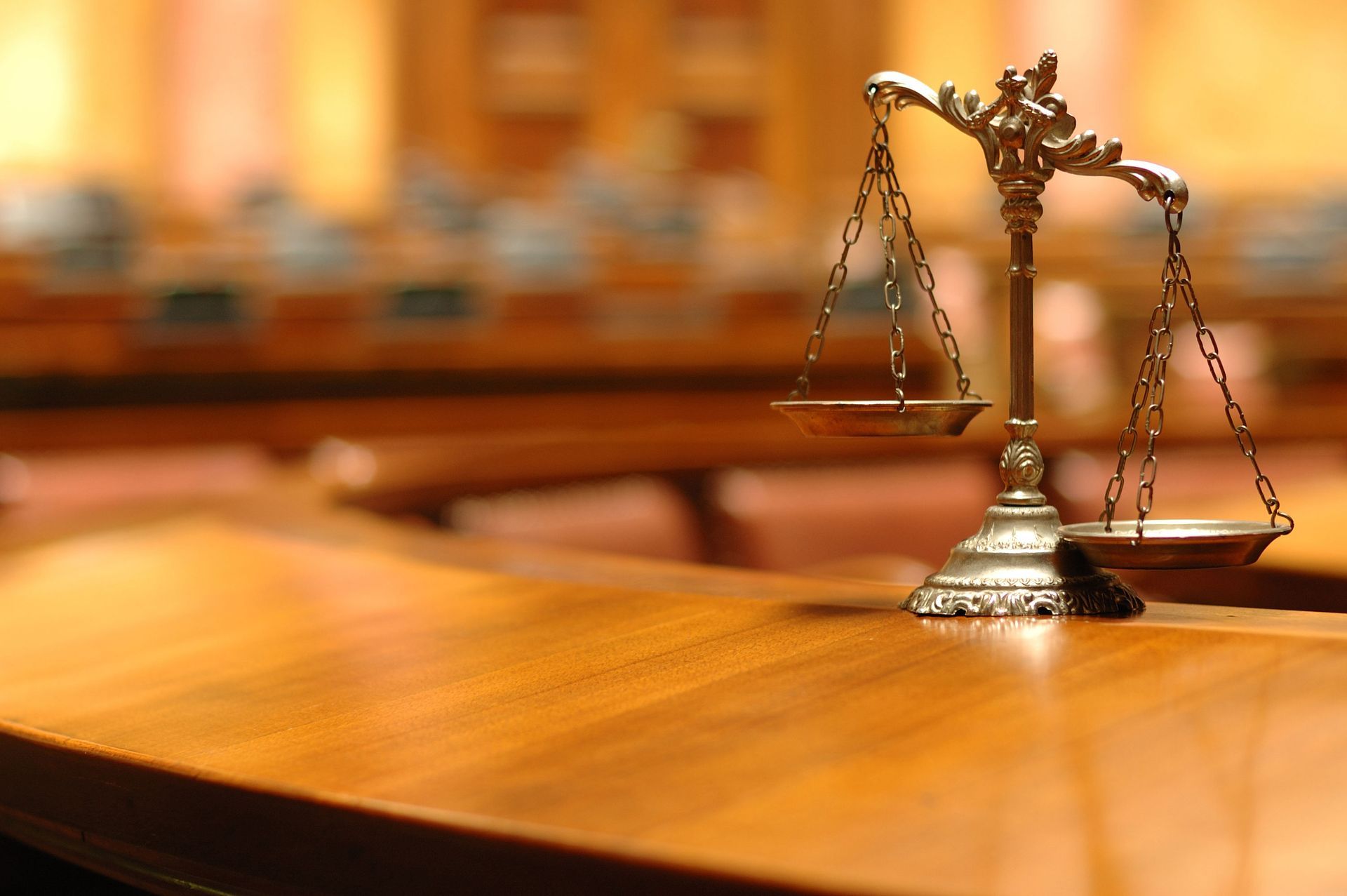 Scales of justice on a wooden table in a blurred courtroom.