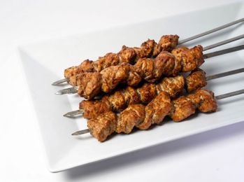 Grilled meat skewers on a white plate, with browned cubes threaded on metal sticks