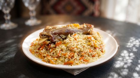 Plate of rice topped with roasted meat and vegetables on a dark table, in soft light