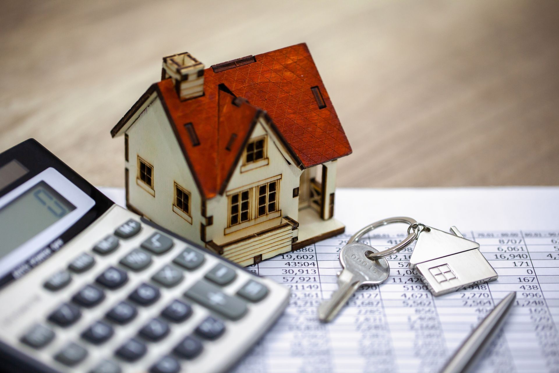 A model house is sitting next to a calculator and keys. A model house is sitting next to a calculator and keys.