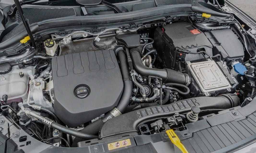 Car engine bay, top-down view. Black engine cover, various components visible.