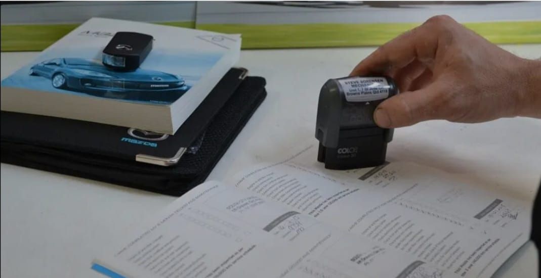 A person's hand holds a black device over a document on a table, with a car key and manual nearby.