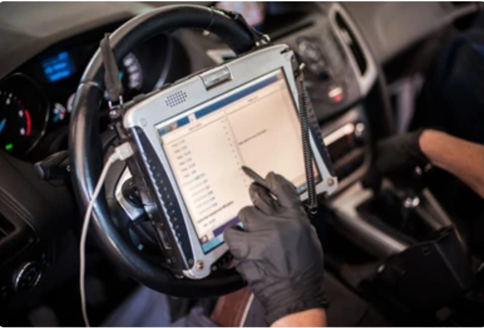 Mechanic using a diagnostic tablet in a car to check engine performance.