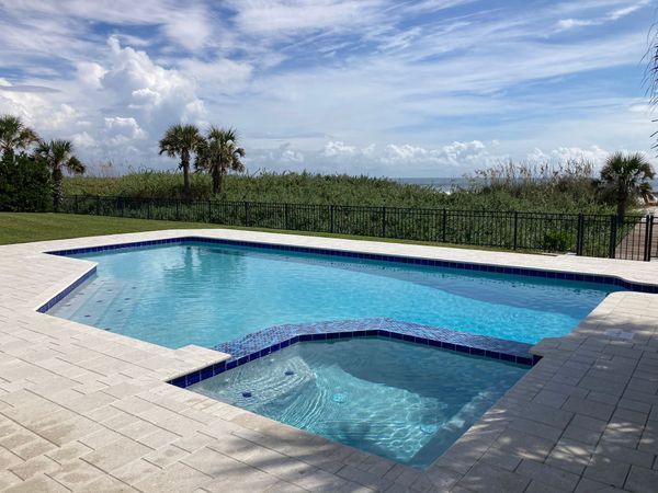 Swimming pool with blue water, surrounded by light-colored stone and overlooking the ocean.