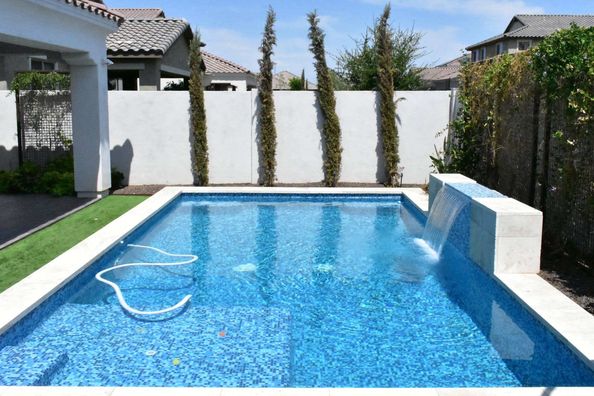 Swimming pool in a sunny outdoor setting surrounded by greenery and a hanging chair under a bright blue sky. Swimming pool in a sunny outdoor setting surrounded by greenery and a hanging chair under a bright blue sky.