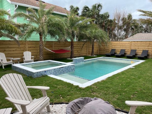 Backyard pool with jacuzzi, palm trees, lawn chairs, and hammock in a fenced yard.